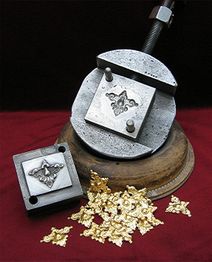 Metallprägeform mit Ornament, umgeben von geprägten goldenen Verzierungen auf rotem Stoff.