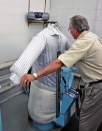 Man using a pressing machine to press a striped shirt in a laundry room.