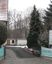 Eingang mit Zaun und Schild im Winter, schneebedeckt, Bäume im Hintergrund.