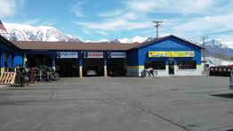 Blue auto repair shop with mountain backdrop; tire displays in front.