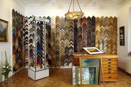 Wand mit diversen Bilderrahmenmustern, Holztisch und Bilder auf dem Boden in einem Geschäft.