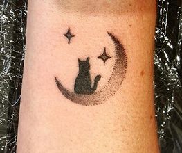 Tattoo van een kat op een halve maan met sterren eromheen op iemands arm.