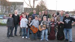 Eine Gruppe von Menschen und Kindern mit Gitarren posiert im Freien.