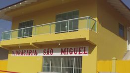 Prédio amarelo com varanda e letreiro "Vidracaria São Miguel" na fachada inferior.