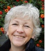 Persoon met grijs haar glimlacht voor bloemenachtergrond.