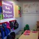Preschool room with coats, backpacks, small chairs, crafts on a table, and a sign on the wall.