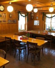 Gemütlicher Gastraum mit Holztischen und Stühlen, dekoriert mit Pflanzen und Wandbildern.