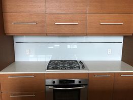Modern kitchen with wooden cabinets, gas stove, white countertops, and a glass backsplash.