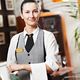 Smiling waitress in uniform with arms crossed, standing in a restaurant setting.