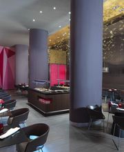Restaurante moderno con mesas negras, sillas oscuras y decoración geométrica en tonos rojos y dorados.