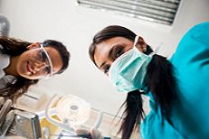 Dentist and assistant wearing masks and goggles, viewed from patient’s perspective.