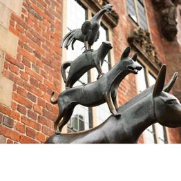 Skulptur der Bremer Stadtmusikanten: Hahn, Katze, Hund und Esel vor roter Backsteinmauer.