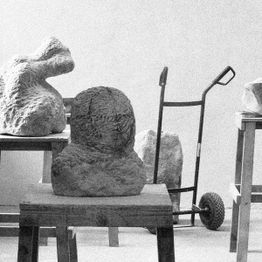 Steinskulpturen auf Tischen und ein Rollwagen im Hintergrund, schwarz-weiß Fotografie.