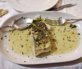 Plato con filete de pescado en salsa verde, acompañado de una cuchara y un tenedor.