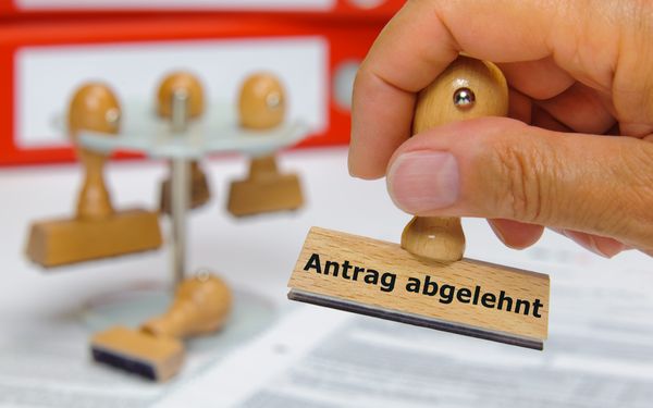 Eine Hand stempelt einen Antrag mit einem Stempel worauf steht "Antrag abgelehnt"."