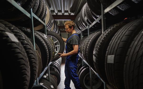 Automechatroniker lagert Sommerreifen in einer großen Lagerhalle, zwischen vielen anderen Reifen, ein.