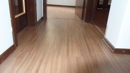 Corredor com piso de madeira clara e portas escuras em ambos os lados.