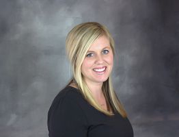 Smiling person with blonde hair and a black top against a gray background.