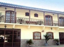 Fachada de casa de dois andares com sacadas, janelas de madeira e plantas ao redor.
