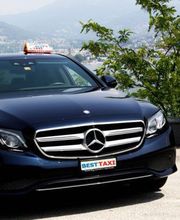 Schwarzes Taxi mit "Best Taxi"-Schild, parkend vor malerischem Hintergrund mit Bergen und Bäumen.