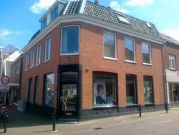 Rood bakstenen hoekpand met grote ramen en een kapperszaak op de begane grond.