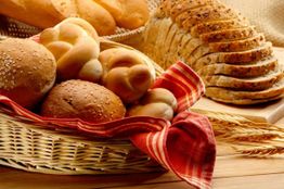 Korb mit verschiedenen Brotsorten, gebettet auf einem roten Tuch, im Vordergrund Weizenähren.