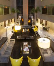 Saguão elegante com sofás cinza, poltronas amarelas e iluminação suave.