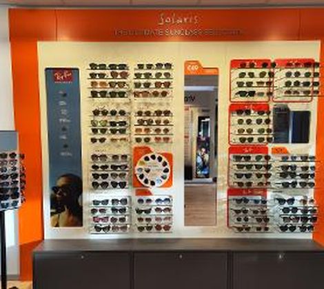 Zonnebrillenwand met diverse modellen in een winkel, tegen een oranje achtergrond.