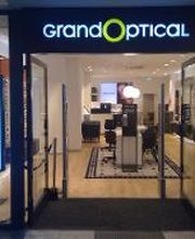 Winkelpui van een opticien met het bord "Grand Optical" en een welkomstdisplay aan de zijkant.