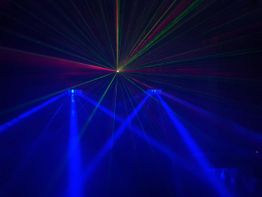 Bunte Laserstrahlen leuchten in einem dunklen Raum und kreuzen sich in der Mitte.