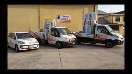 Veicoli commerciali bianchi con il logo dell'azienda, parcheggiati all'esterno di un edificio giallo.