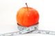 Roter Apfel mit Maßband umwickelt, Symbol für gesunde Ernährung.