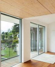 Camera moderna con vetrate ampie, parquet, letto colorato e vista su giardino verde.