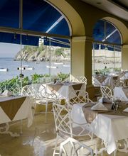 Restaurante con mesas junto al mar, vista de barcos y ventanas grandes, decoración elegante.