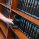 Hand pulling a book from a shelf filled with dark blue encyclopedias.
