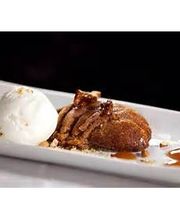 Postre en un plato: helado de vainilla junto a un pastel con salsa de caramelo y nueces.