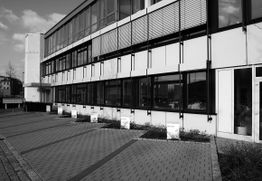 Moderner Bürogebäudekomplex mit großen Fenstern und gepflastertem Weg, schwarz-weiß dargestellt.