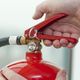 Hands holding a red fire extinguisher, focusing on the handle and pin.