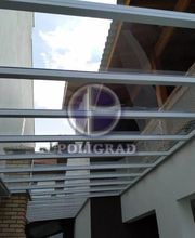 Cobertura transparente entre edifícios, estrutura de metal branco e céu ao fundo.