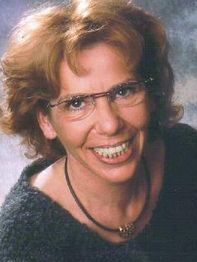 Eine Frau mit Brille und einem freundlichen Lächeln vor grauem Hintergrund.