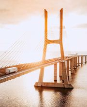 Puente sobre el agua iluminado por el sol al atardecer, con un camión cruzando.