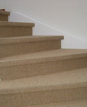 Braune, mit Teppich belegte Treppe mit weißem Geländer, die um die Ecke führt.