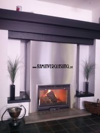 Moderner Kamin mit Glasfront, flankiert von Grünpflanzen auf schwebenden Regalen.