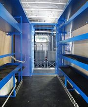 Innenraum eines Lieferwagens mit blauen Regalen und einem Gitter zwischen Laderaum und Fahrerraum.