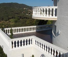 Weiße Terrasse mit Balustraden vor bewaldeten Hügeln und blauem Himmel.