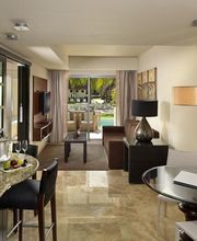 Sala moderna con cocina, mesa de vidrio y vista al balcón. Muebles elegantes y lámpara colgante.