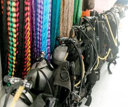 Equipos de buceo y tanques de oxígeno junto a coloridas cuerdas colgadas en la pared.