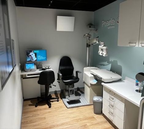 Kleine optometrieruimte met stoel, bureau, computer en oogmeetapparatuur.