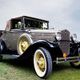 Classic vintage car with yellow wheels on grass under a cloudy sky.
