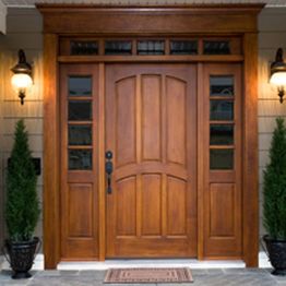 Wooden front door with glass panels, flanked by two decorative lanterns and plants.